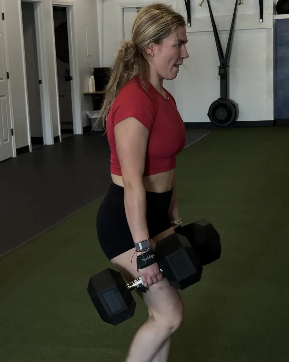 Athlete carrying heavy dumbbells across the turf
